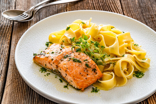 Pasta with baked salmon steak on wooden table
