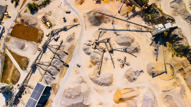 Aerial view of sand quarry processing plant with conveyor belts. Overhead shot displays industrial equipment, aggregate piles and solar panels on roof.