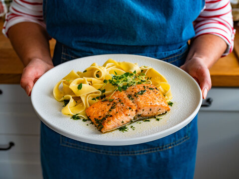 Woman holding plate with pasta with baked salmon steak, close-up

