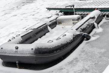 Snow covered inflatable boat moored beside frozen dock on winter water © Ernest