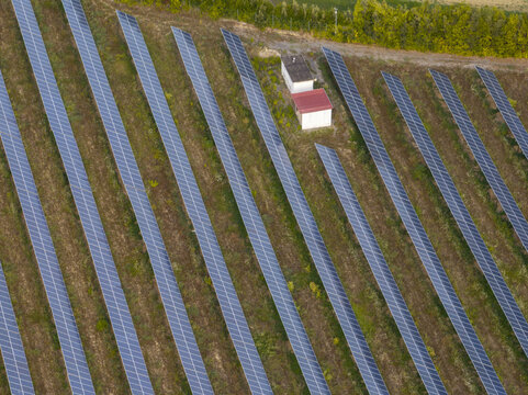 Aerial view of a solar farm with rows of photovoltaic panels arranged in a field with a small utility building in Fermo, Marche, Italy.
