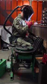 Vertical video of male welder in protective gear welding metal parts at workbench in workshop. Footage is ideal for industrial manufacturing and vocational training promotions