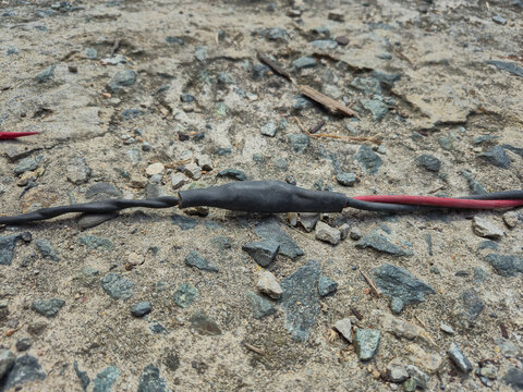 Electrical Cable Wire Splicing with Black Shrink Tube Insulation on Rough Concrete Surface for Power Connection Repair