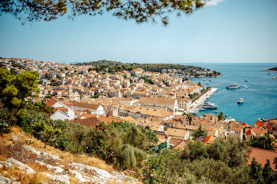View of Hvar Port with historic stone buildings, terracotta rooftops, and boats docked in the clear blue Adriatic Sea in Hvar, Split-Dalmatia County, Croatia.