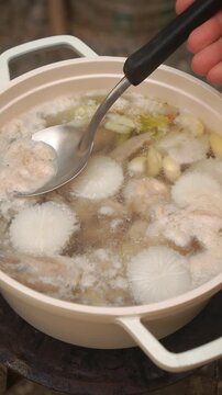 Cooking Thai chicken soup with dried daylilies (Dok Mai Cheen). Boiling chicken legs with radish, garlic, shiitake mushrooms, and daylilies until clear and aromatic.
