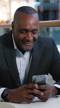 Joyous 50s mature African American business man using mobile phone receiving good email notification email satisfied shaking head businessman male browsing gadget working with smartphone at cafe table