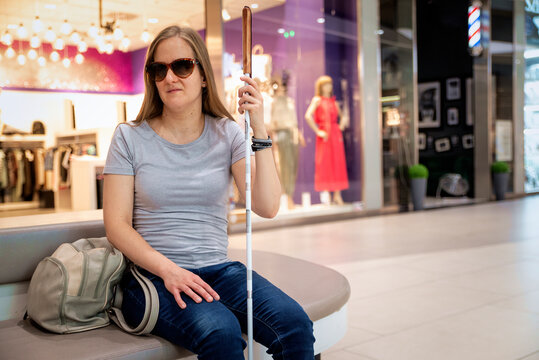 Confident blind woman with white cane sitting on a bench in a shopping mall