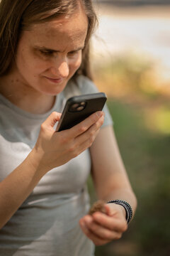 Visually impaired woman holding a pine cone in her hand and using a specialized accessibility app on her smartphone outdoors