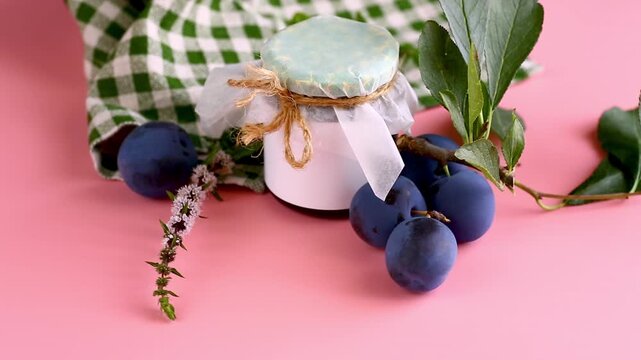 Homemade plum preserve with ripe plums on pastel pink background