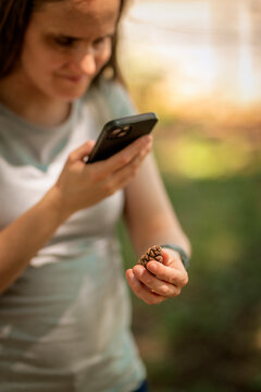 Visually impaired woman holding a pine cone in her hand and using a specialized accessibility app on her smartphone outdoors