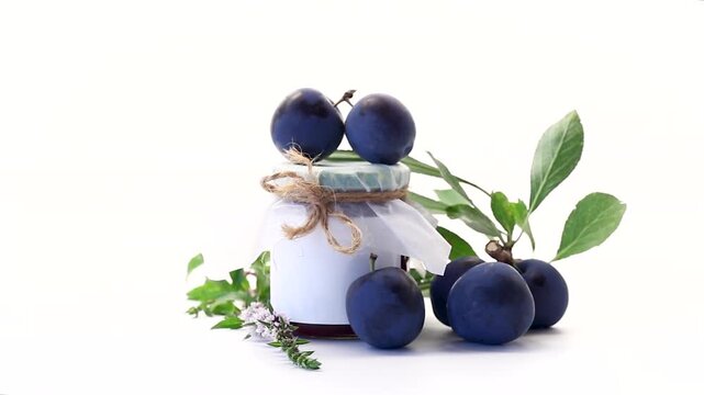 Rustic plum preserve in jar surrounded by ripe plums and herbs