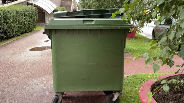  Green wheeled waste bins standing on a pavement near a residential building outdoors, waste collection, recycling, urban cleanup.