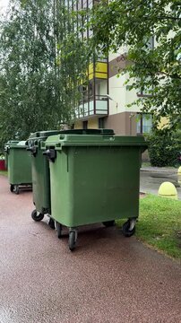  Green wheeled waste bins standing on a pavement near a residential building outdoors, waste collection, recycling, urban cleanup.