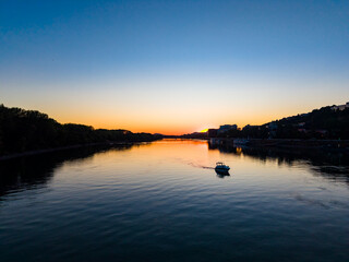 Obraz premium Sunset over the river with a boat sailing in the calm waters near the shoreline