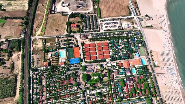 Aerial view of holiday resort with swimming pools, sports courts, and rows of bungalows located along the sandy coastline in Porto San Giorgio, Marche, Italy.