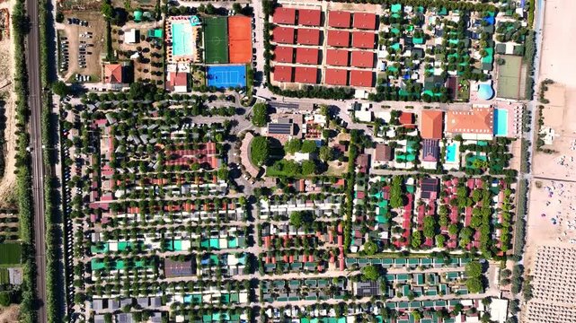 Aerial view of a holiday resort featuring swimming pools, sports courts, and rows of bungalows nestled among trees in Porto San Giorgio, Marche, Italy.