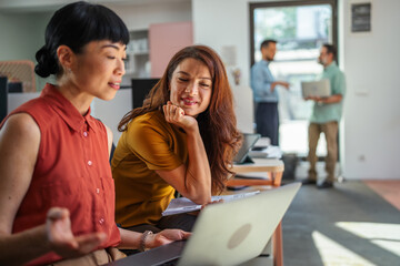 Fototapeta premium Diverse businesswomen collaborating on laptop in modern office