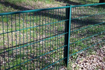 Clôture en panneaux de grillage rigide à double fil de couleur verte, installée sur des poteaux métalliques pour délimiter un espace extérieur. © CURIOS