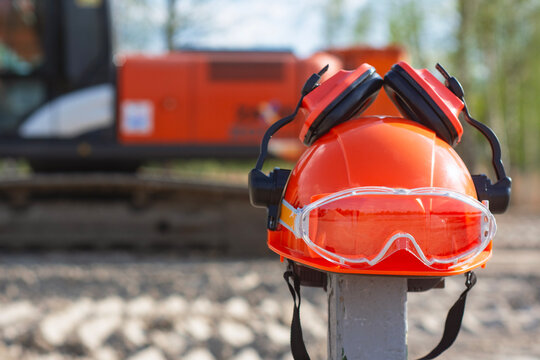 Orange safety helmet with protective goggles and earmuffs placed at a construction site, representing workplace safety, protective equipment, industrial work, building and occupational health.