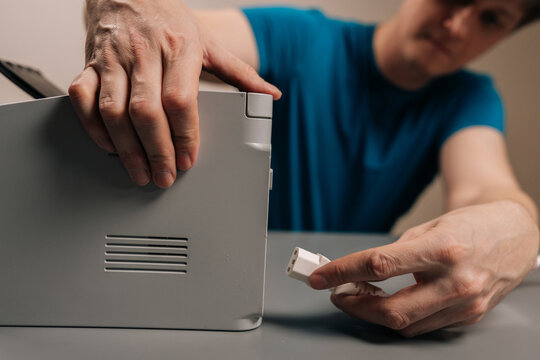 Focused man connecting power supply cable to a printer, setting up new office equipment for home or business use, focusing on electronic hardware installation and technology.