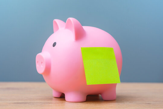 Pink piggy bank with a blank green note on a wooden table, representing savings, personal finance, budgeting, money management and financial planning with copy space.