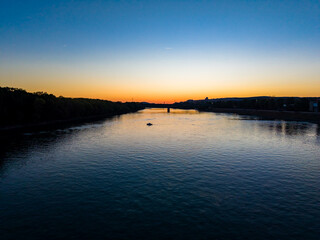 Fototapeta premium River at sunset with a small boat in the water and hills in the background near a city along the riverbank