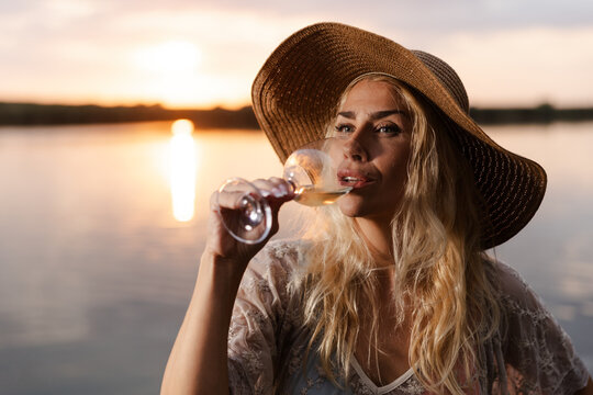 Woman Enjoys a Drink by the River During Summer While Watching the Sunset