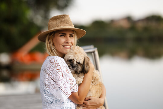Woman Holds Dog by River in Summer Near a Boat