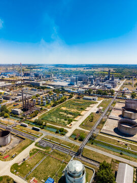 Industrial site view showing factories, storage tanks, and a clear sky in the background with open land area nearby