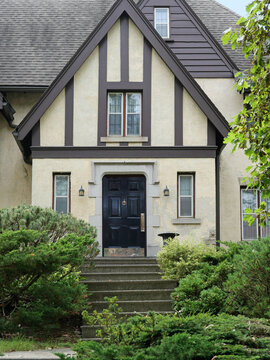 Front door and front steps of old Tudor style stucco house, surrounded by shrubbery