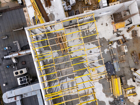 Aerial view of a construction site featuring yellow formwork beams, concrete slabs, and building materials arranged on the ground in Gdansk, Poland.