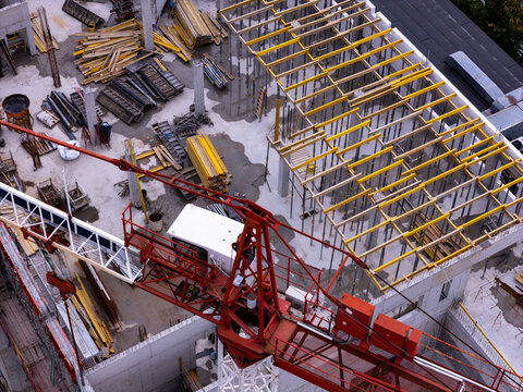 Aerial view of a construction site featuring a prominent red tower crane, steel scaffolding, and various building materials on a concrete foundation in Gdansk, Poland.