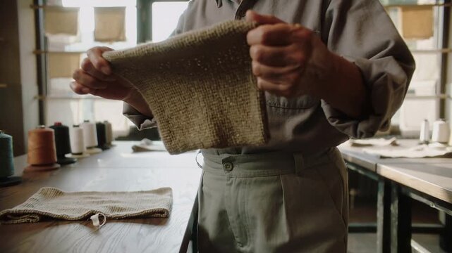 Approaching table senior maker in rolled sleeves picking up swatch testing drape at studio, cones