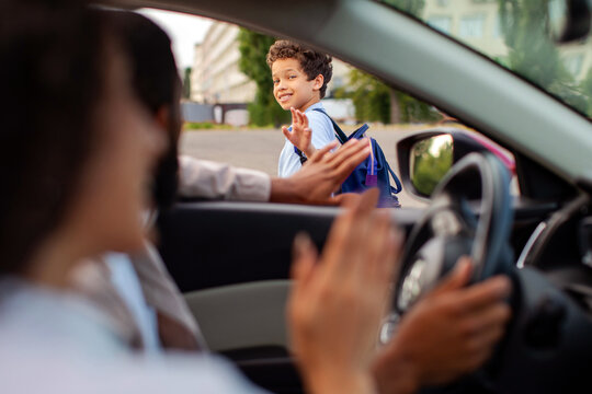 Smiling schoolboy waving goodbye to parents from outside car before heading school