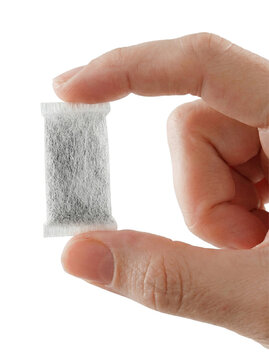 Hand Holding Single Portion Tobacco Free Nicotine Pouch. Close up of a hand holding a white portion bag of nicotine pouch or snus over white background.