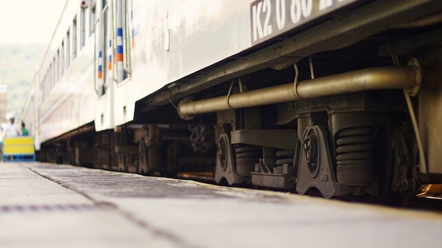 Low angle close-up of a passenger train undercarriage and bogie wheels at a station platform