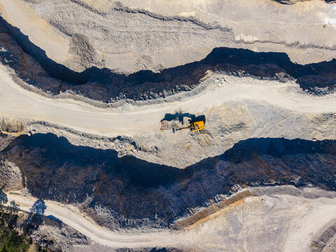 Construction activity happens in a mine, where large machines move dirt and rocks to extract resources, taking place in a remote area under clear skies