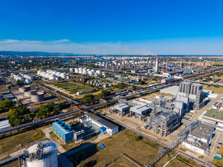 Fototapeta premium Factory and industrial complex seen from above with storage tanks and pipelines in an urban area during clear daylight