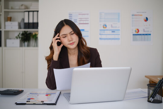 Young Asian businesswoman discussing work by phone at her office desk.