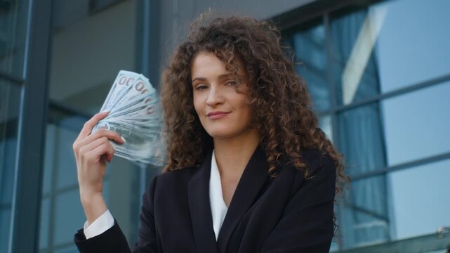 Happy rich Caucasian business woman holding money waving fan with cash looking at camera smiling cheerful businesswoman female girl agent with dollars finance wealth investment in city near office