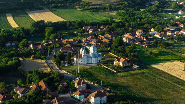 Aerial view of a church surrounded by houses, green fields, and trees in Deva, Hunedoara, Romania.