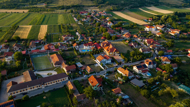 Aerial view of a rural village with red-roofed houses, agricultural fields, and a sports court in the countryside of Deva, Hunedoara, Romania.