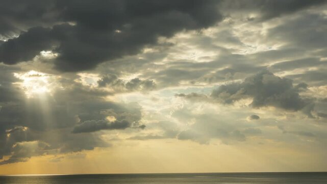 Time-lapse of dramatic sunset over the ocean with sun rays piercing through moving clouds at golden hour