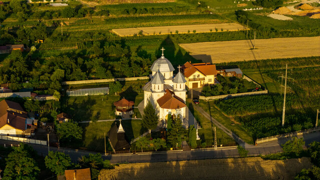 Aerial view of an Orthodox church with a silver dome surrounded by green fields and rural houses in Deva, Hunedoara, Romania.