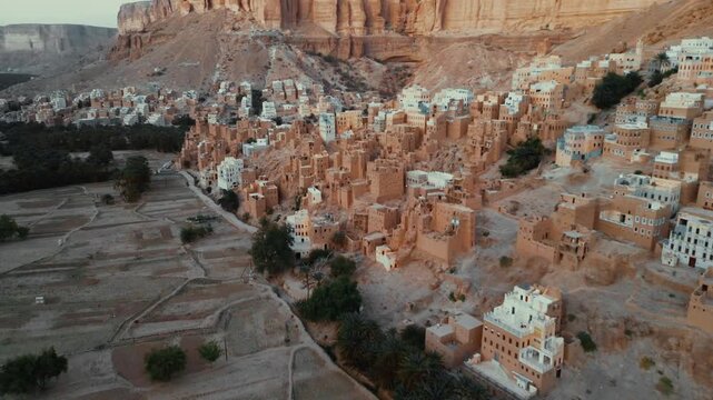 Aerial view of the historic mud-brick village of Al-Hajarayn, featuring traditional architecture built into the rocky cliffside of the Wadi Dawan region in Alhajrain, Hadhramaut Governorate, Yemen.