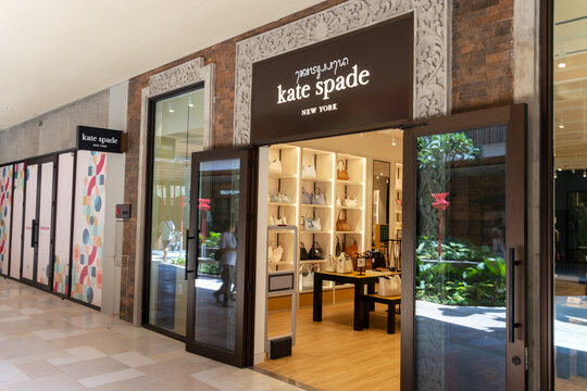 Sira village mall, Bali, Indonesia, August 16,2026: Illuminated Kate Spade storefront with carved stone frame, open glass doors, and luxury handbag displays at a modern outlet mall.