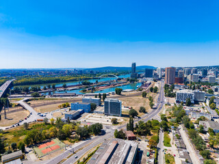 Fototapeta premium View of a city area with buildings, a river, and roads under a clear sky, showing urban development and open spaces