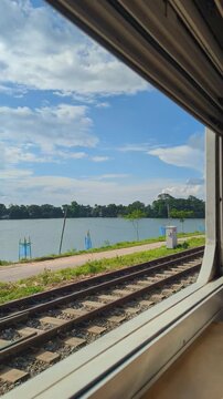 View From Train Window Showing Parallel Railway Tracks and Lake Under Blue Sky