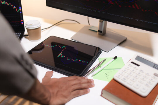 Professional trader analyzing stock market charts on laptop, tablet, and monitor while reviewing candlestick patterns, technical indicators, and market trends to support informed investment decisions.