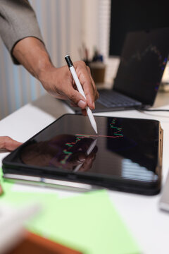 Professional financial analyst reviewing stock market charts across multiple screens using a tablet, laptop and calculator to evaluate price movements, technical indicators, and investment strategies.